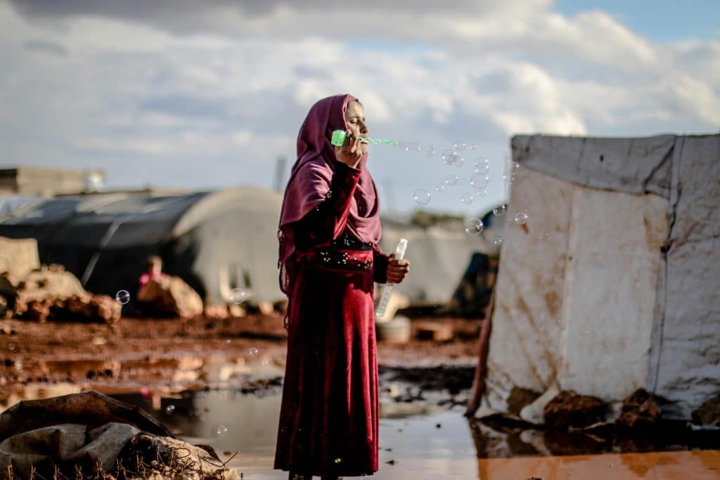 A woman in a hijab blows soap bubbles in a Syrian refugee camp in Idlib.